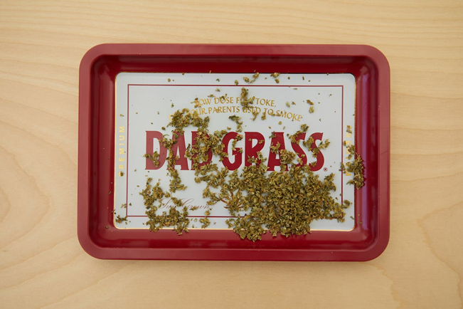 a red tray on a wooden table with cannabis scraps on it